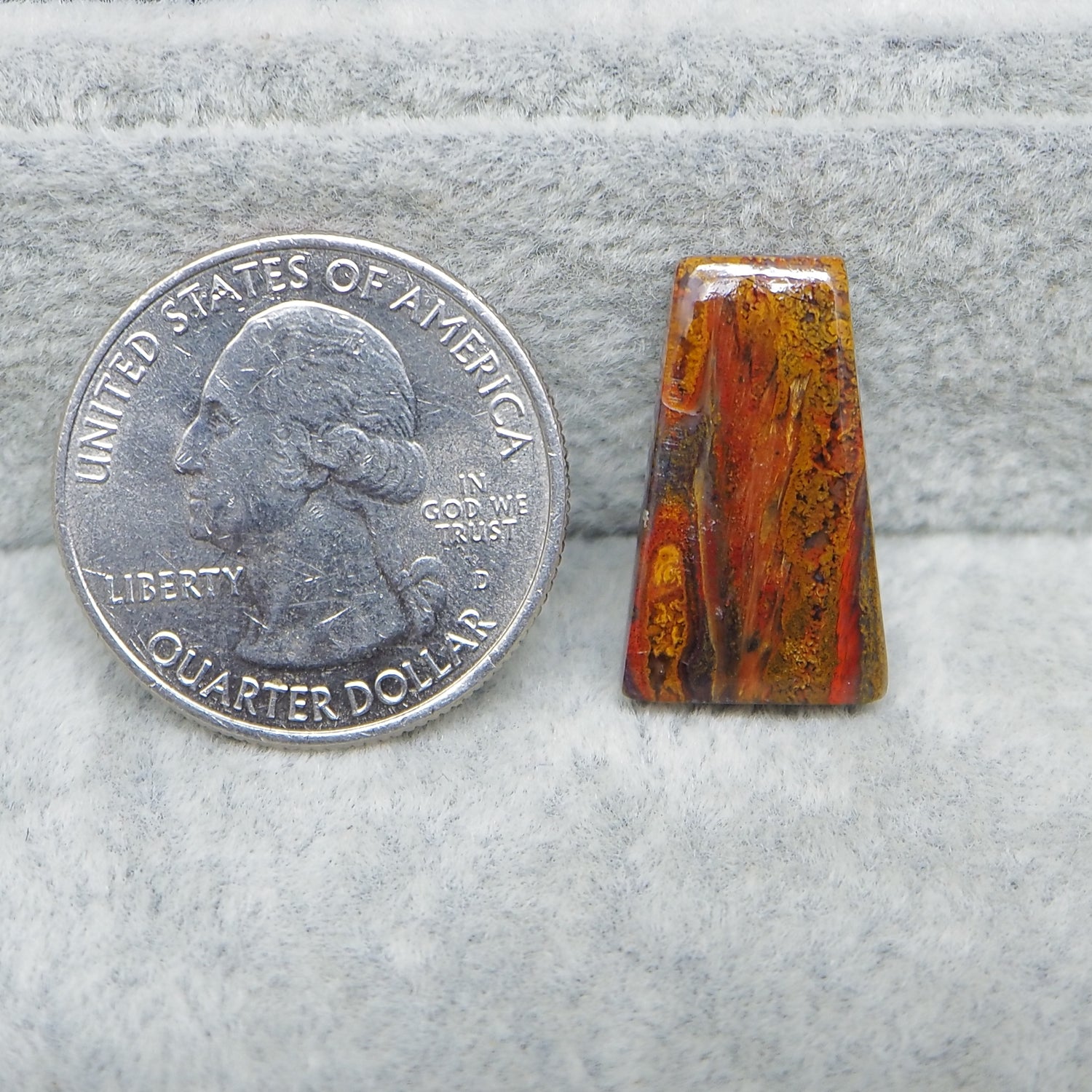 Small amber stone next to a U.S. quarter dollar on a gray surface
