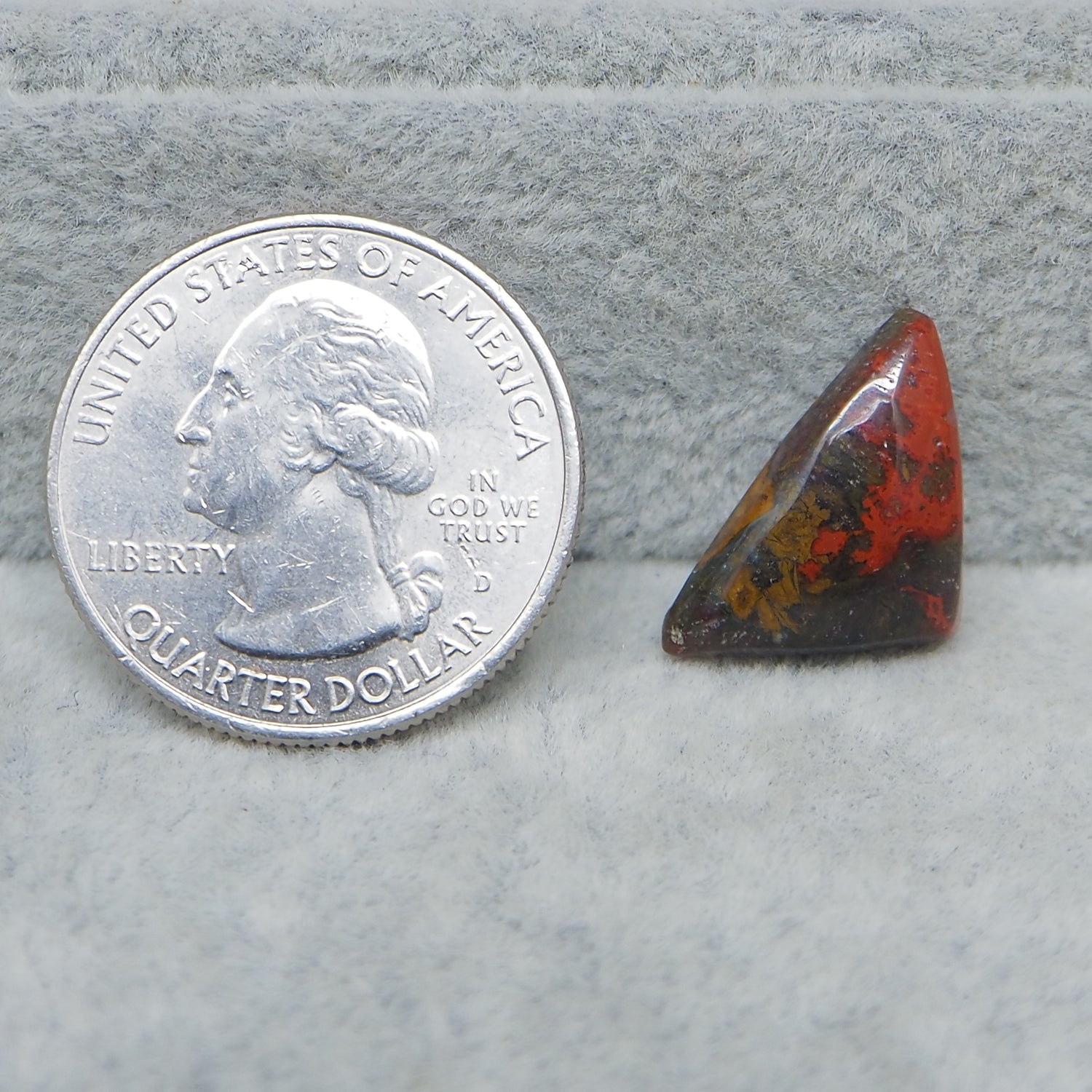 Quarter dollar coin next to a triangular red and brown stone on a gray surface