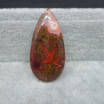 Teardrop-shaped red and brown agate stone on a gray surface