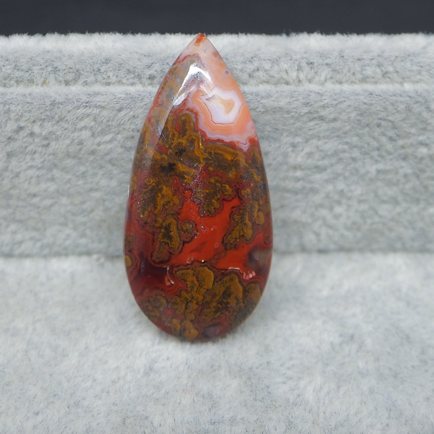 Teardrop-shaped red and brown agate stone on a gray surface