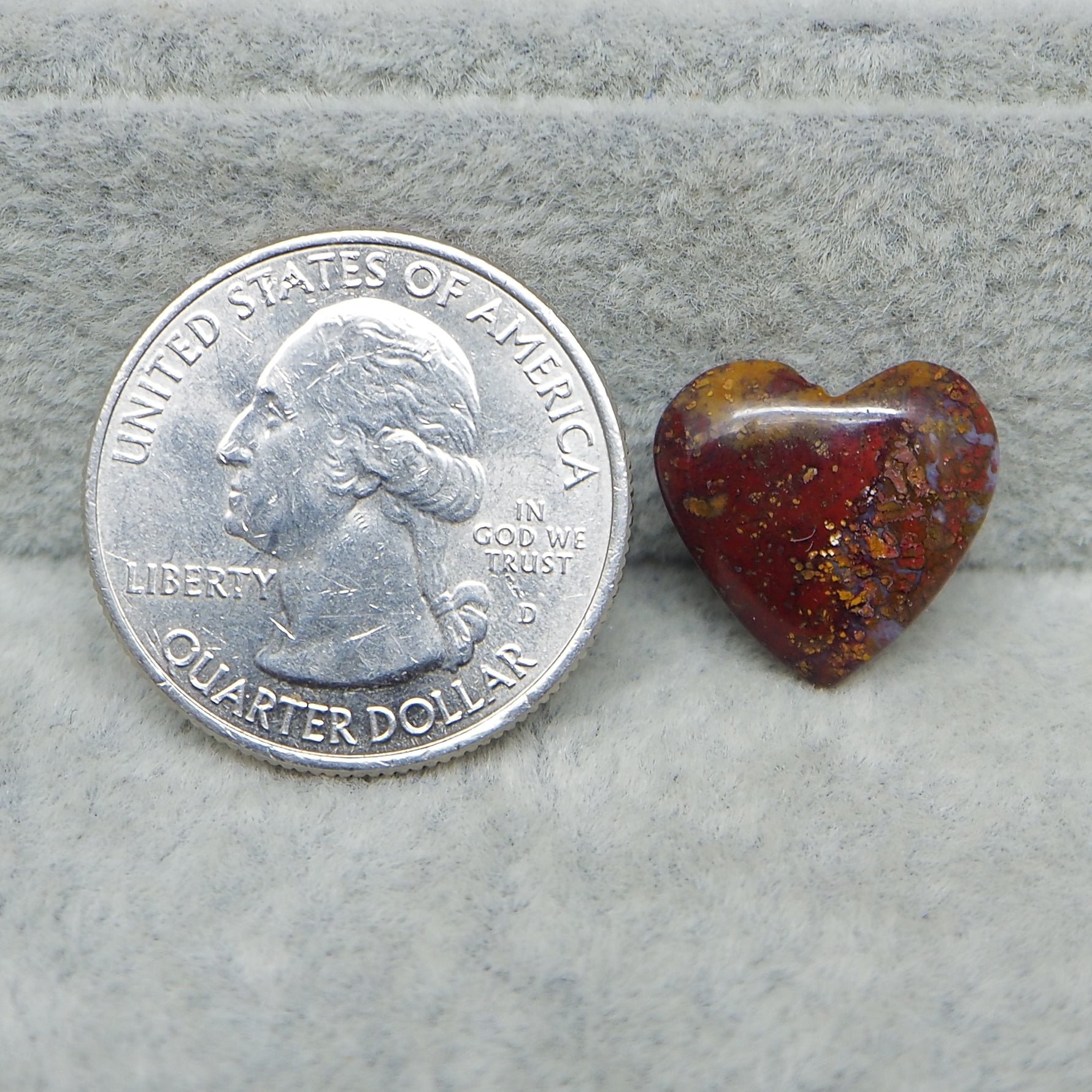 Heart-shaped Seam Agate stone next to a U.S. quarter dollar on a gray surface
