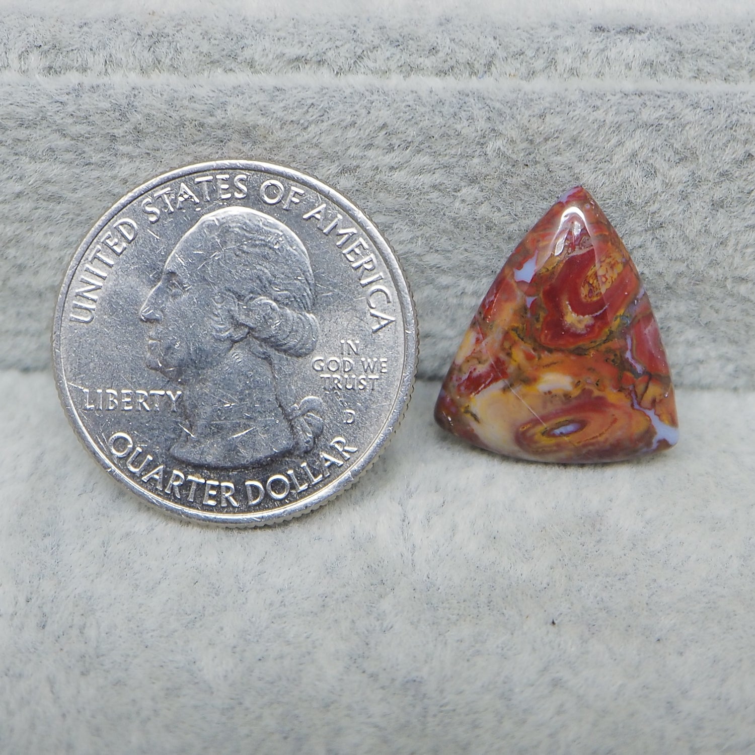 Quarter dollar coin next to a colorful triangular stone on a gray surface