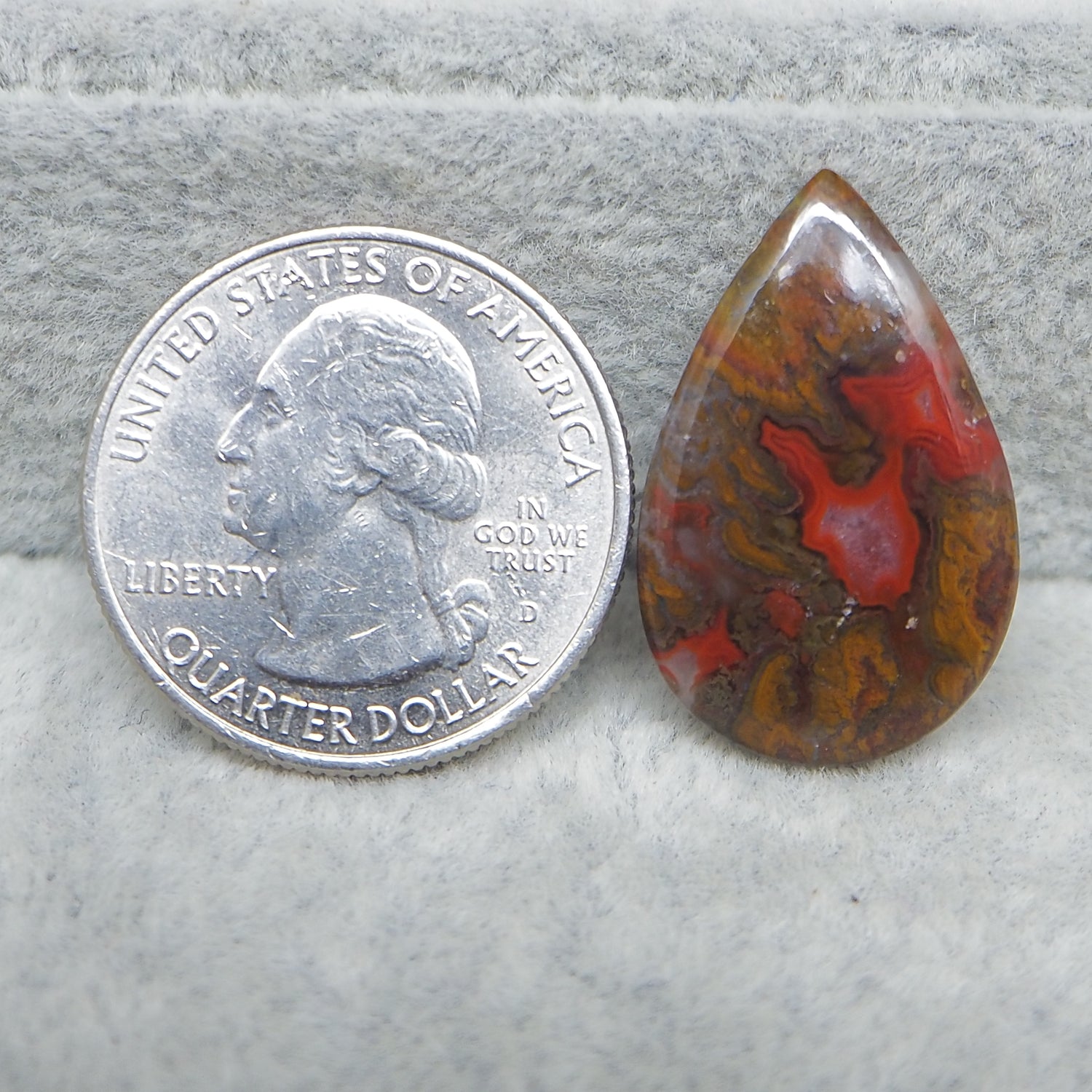 Teardrop-shaped jasper stone next to a U.S. quarter dollar coin on a gray surface.
