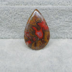 Teardrop-shaped jasper stone with red and brown patterns on a gray surface