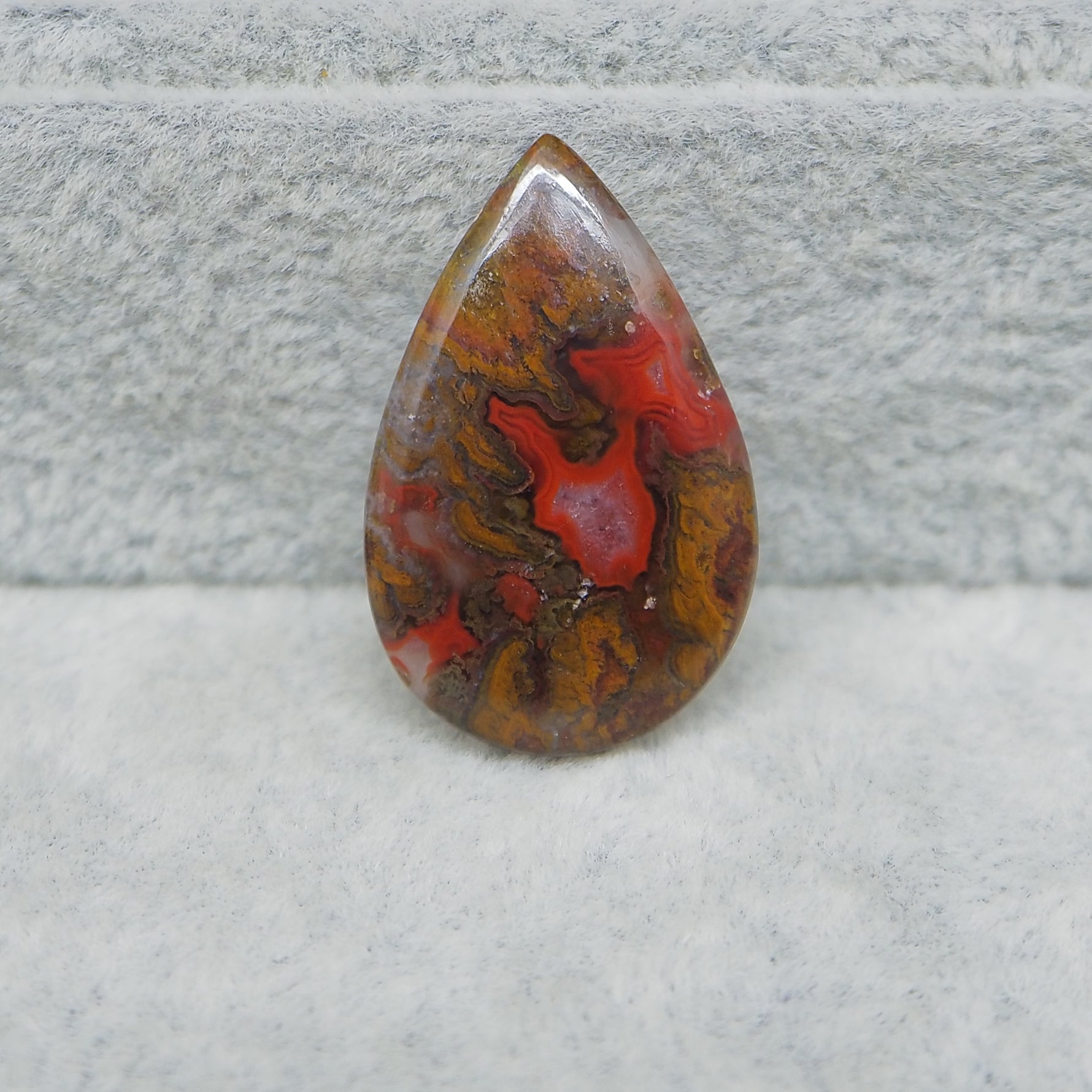 Teardrop-shaped jasper stone with red and brown patterns on a gray surface