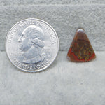 Quarter dollar coin next to a triangular piece of red and brown stone on a gray surface