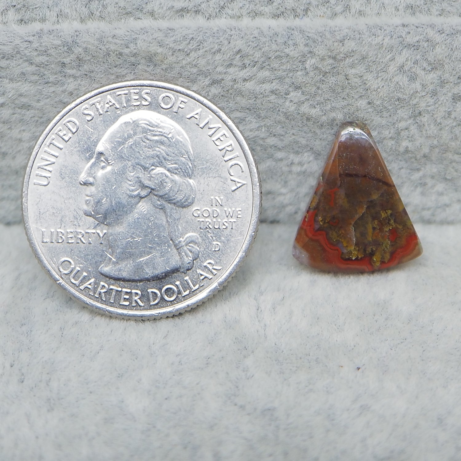 Quarter dollar coin next to a triangular piece of red and brown stone on a gray surface