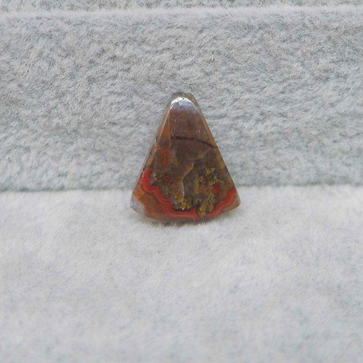 Triangular stone with red and brown colors on a gray surface