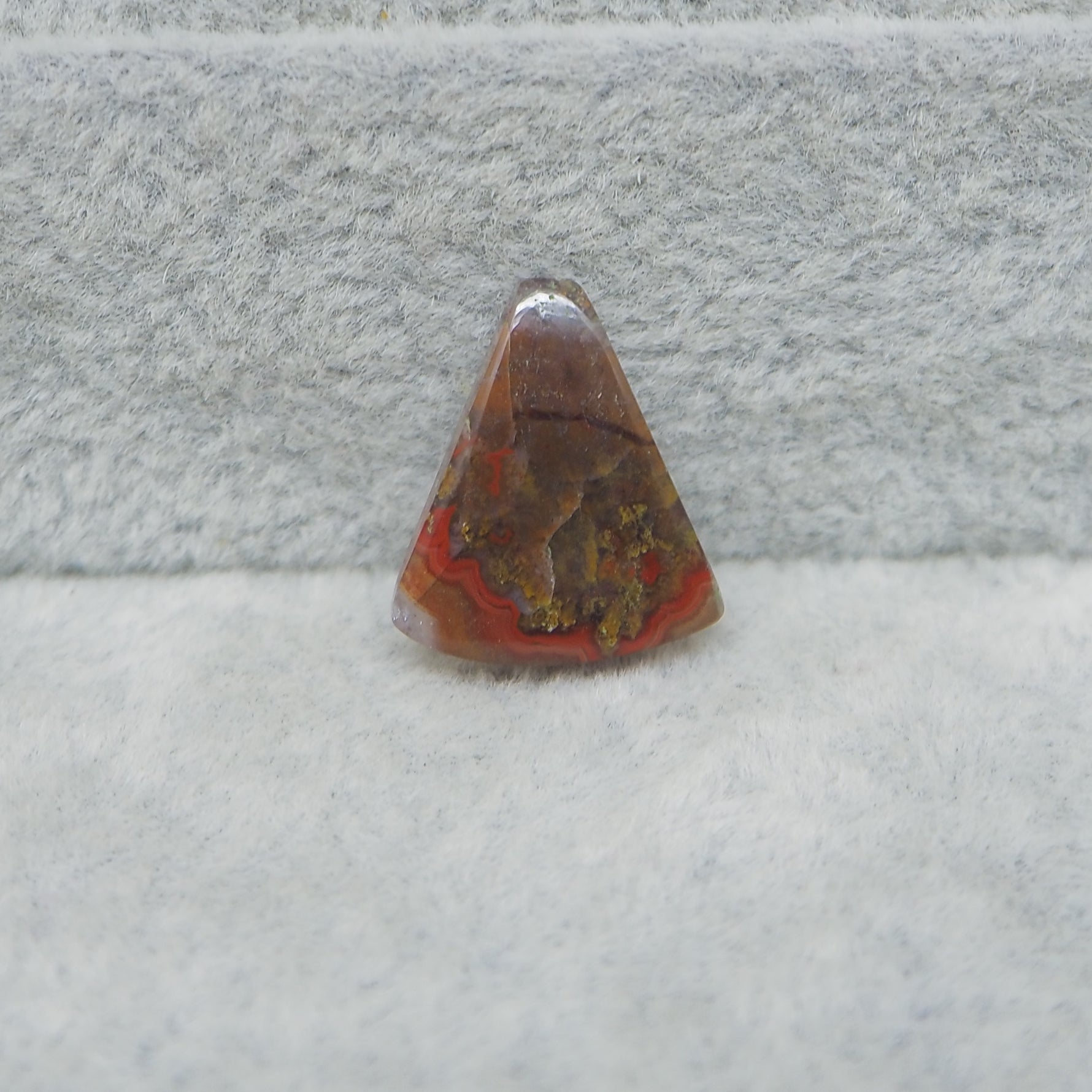 Triangular stone with red and brown colors on a gray surface