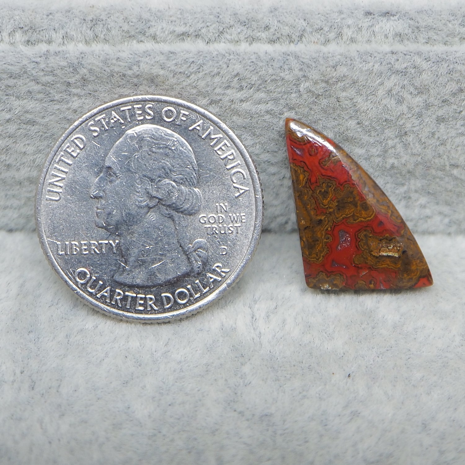 Quarter dollar coin next to a red and brown stone on a gray surface