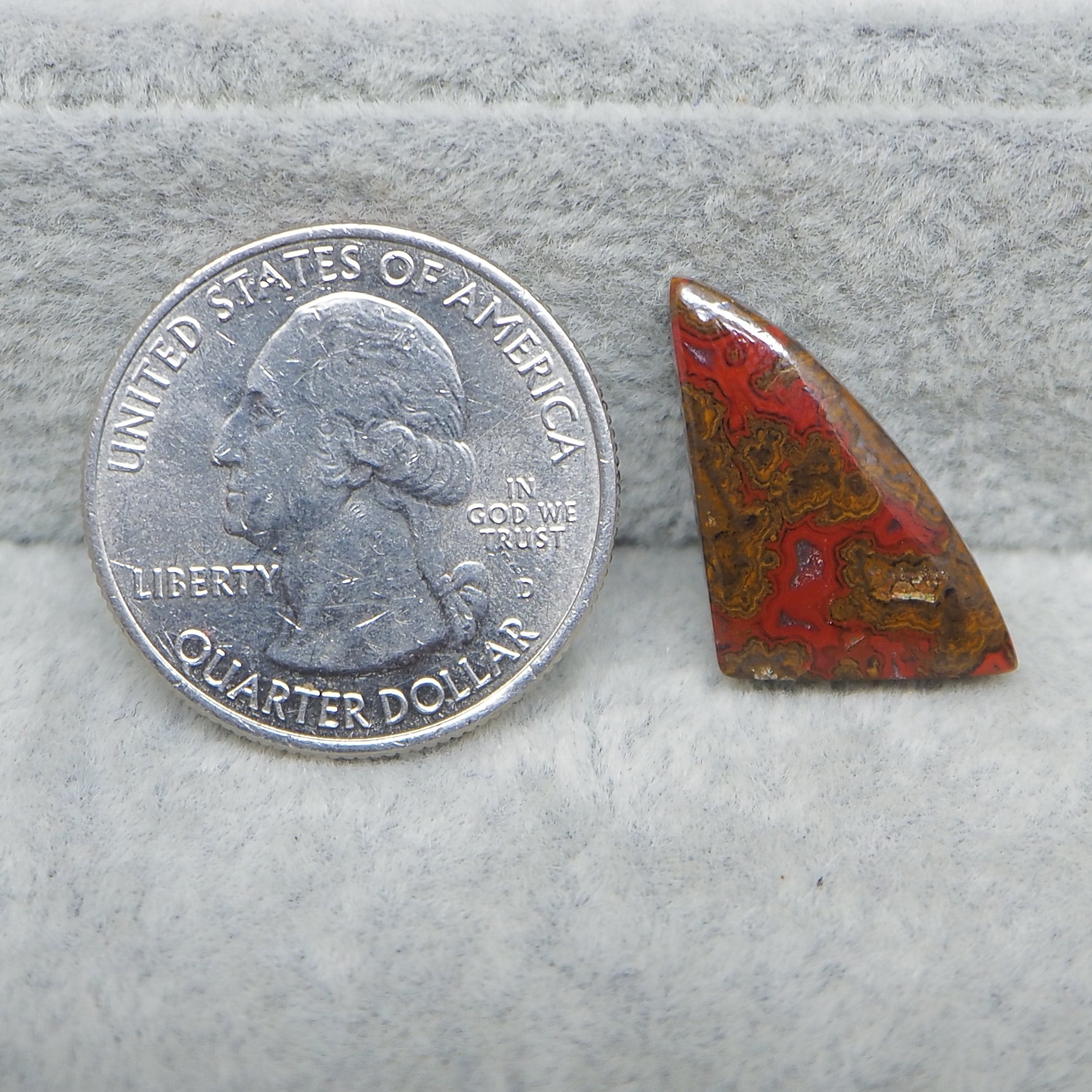 Quarter dollar coin next to a red and brown stone on a gray surface