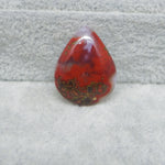 Red teardrop-shaped stone on a textured gray surface