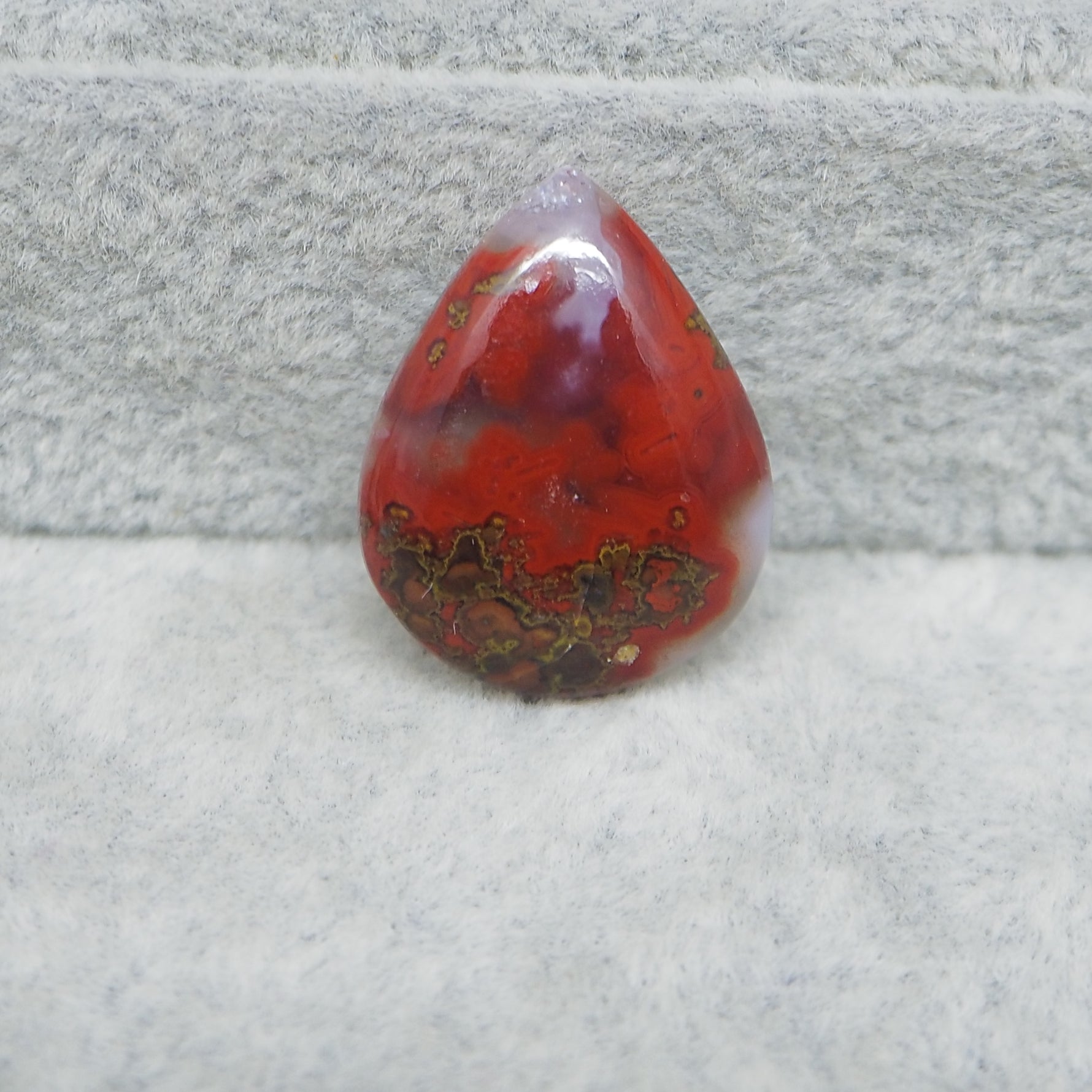 Red teardrop-shaped stone on a textured gray surface