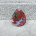 Teardrop-shaped gemstone with red, brown, and white patterns on a textured gray background