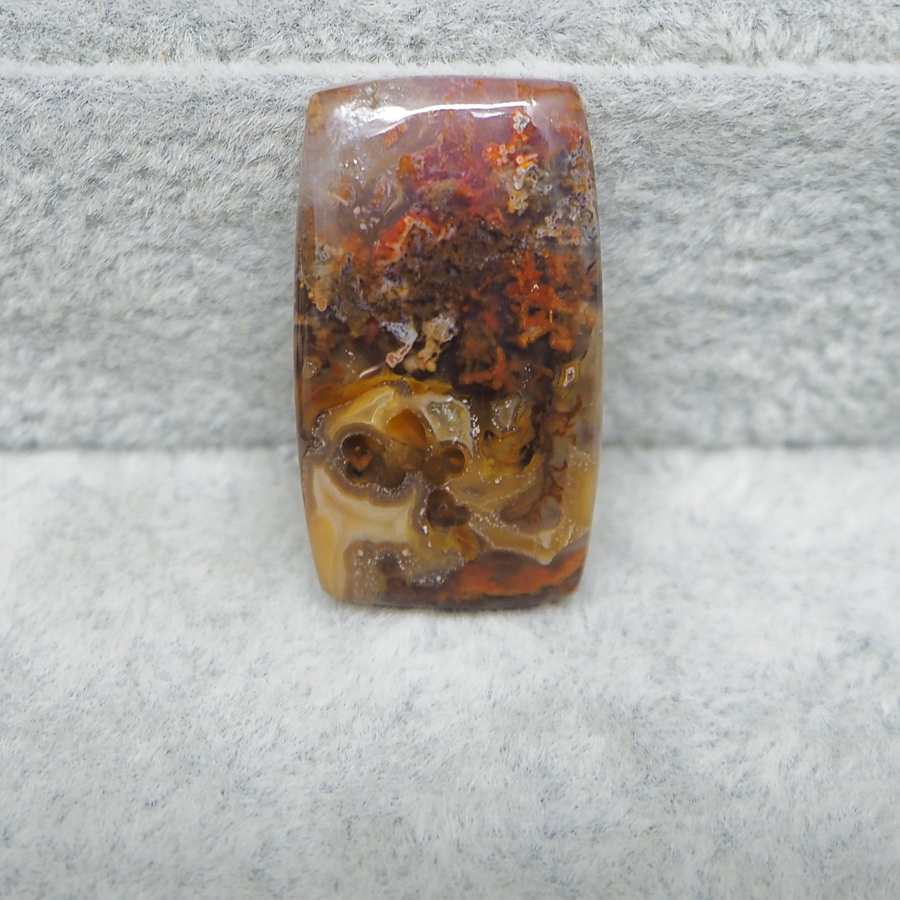 Rectangular stone with brown, orange, and yellow patterns on a gray surface