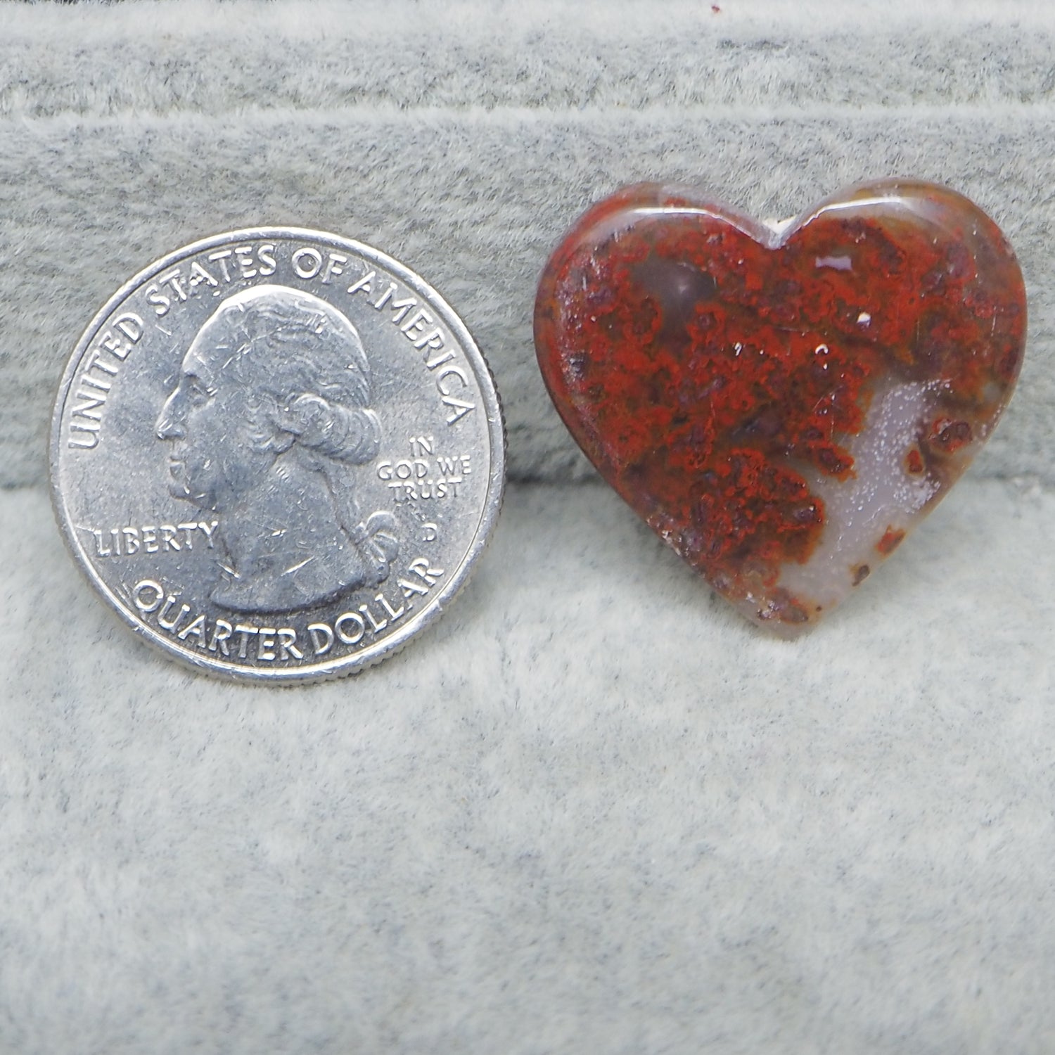 Heart-shaped red and brown stone next to a U.S. quarter dollar on a gray surface