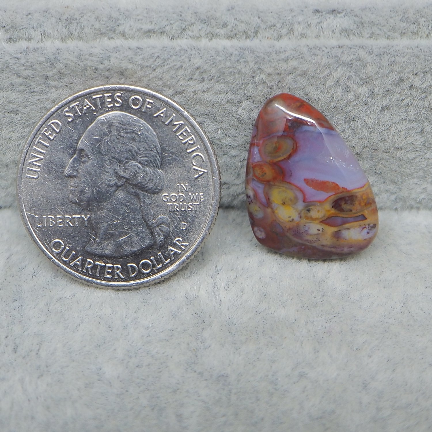 Colorful marbled stone next to a U.S. quarter dollar on a gray surface