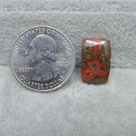 Quarter dollar coin next to a red and brown stone on a gray surface