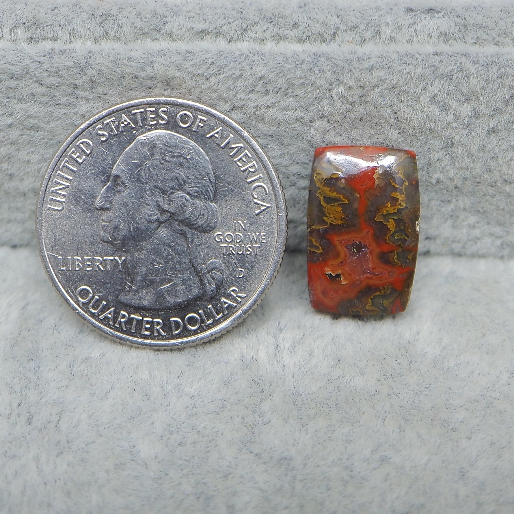 Quarter dollar coin next to a red and brown stone on a gray surface