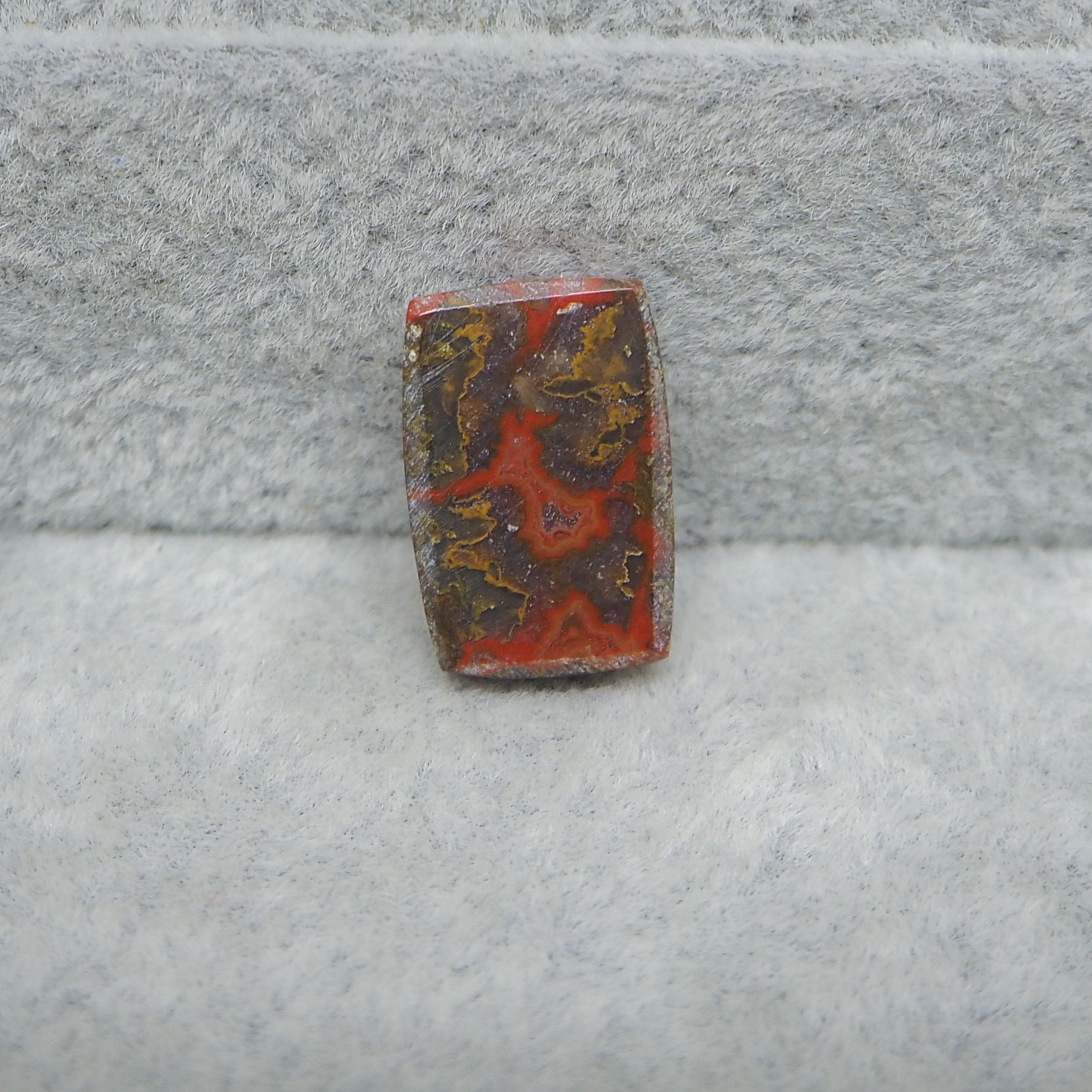 Rectangular stone with red and brown patterns on a gray textured background