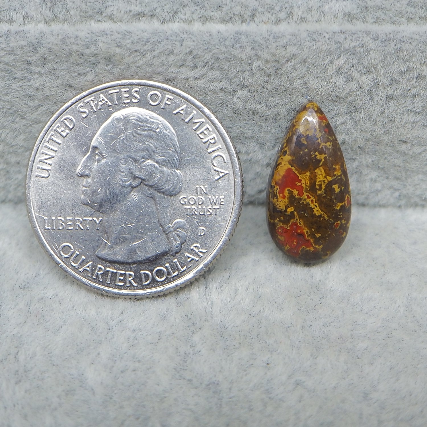 Quarter dollar coin next to a teardrop-shaped amber stone on a gray surface