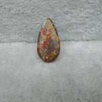Teardrop-shaped stone with red and yellow patterns on a gray surface