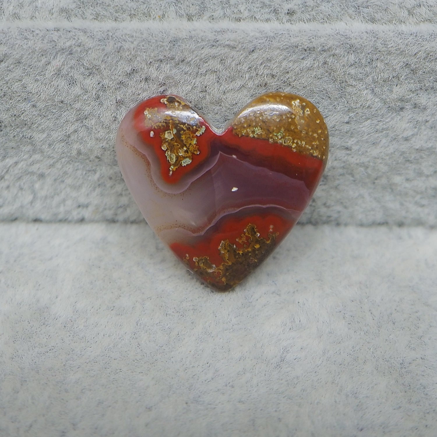 Heart-shaped agate stone with red and gold patterns on a gray surface