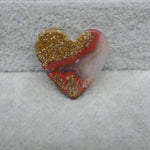 Heart-shaped stone with gold and red patterns on a gray surface