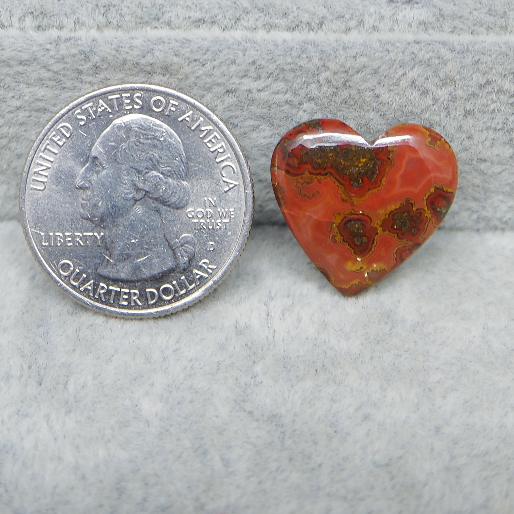 Heart-shaped red and brown stone next to a U.S. quarter dollar on a gray background