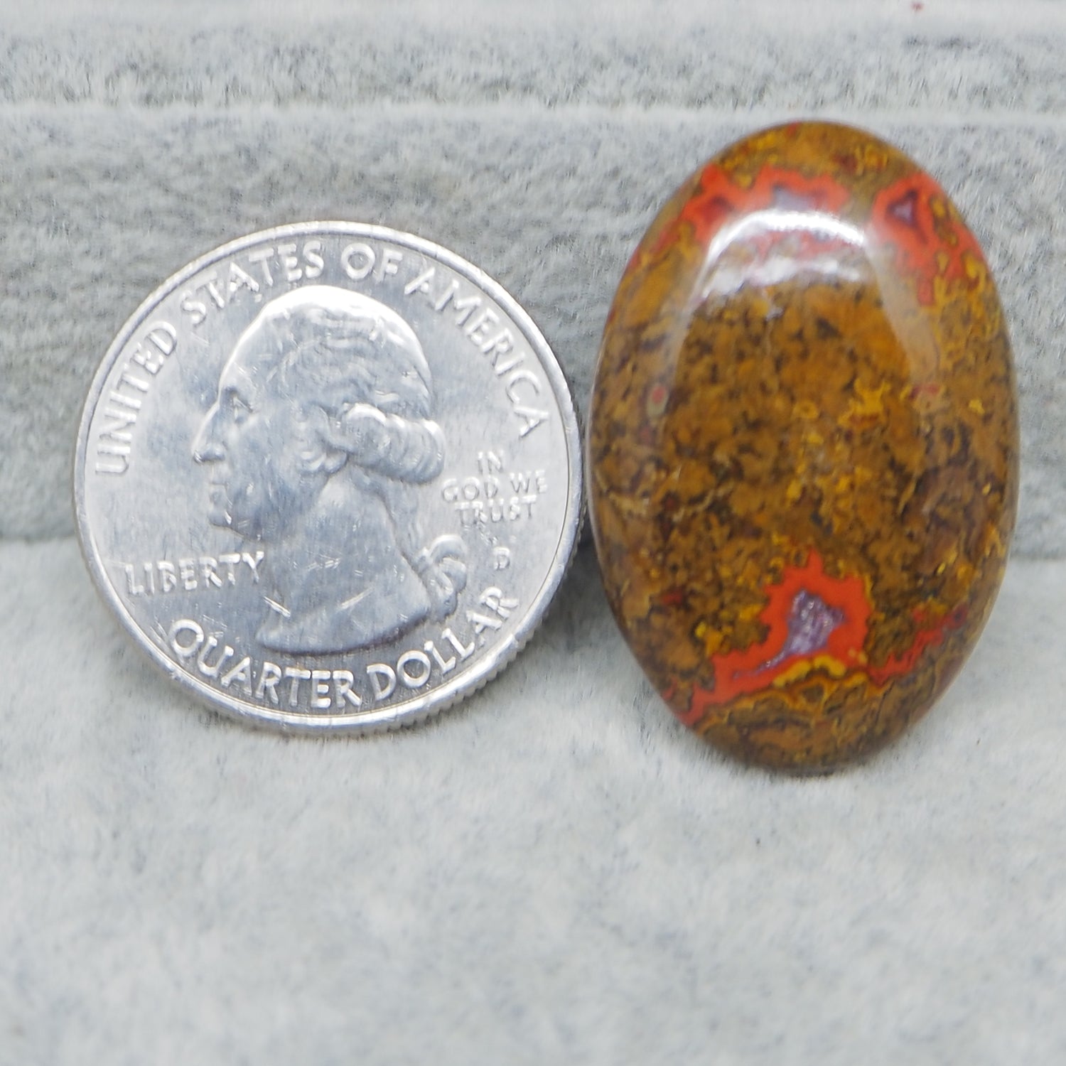 Quarter dollar coin next to a colorful oval stone on a gray surface