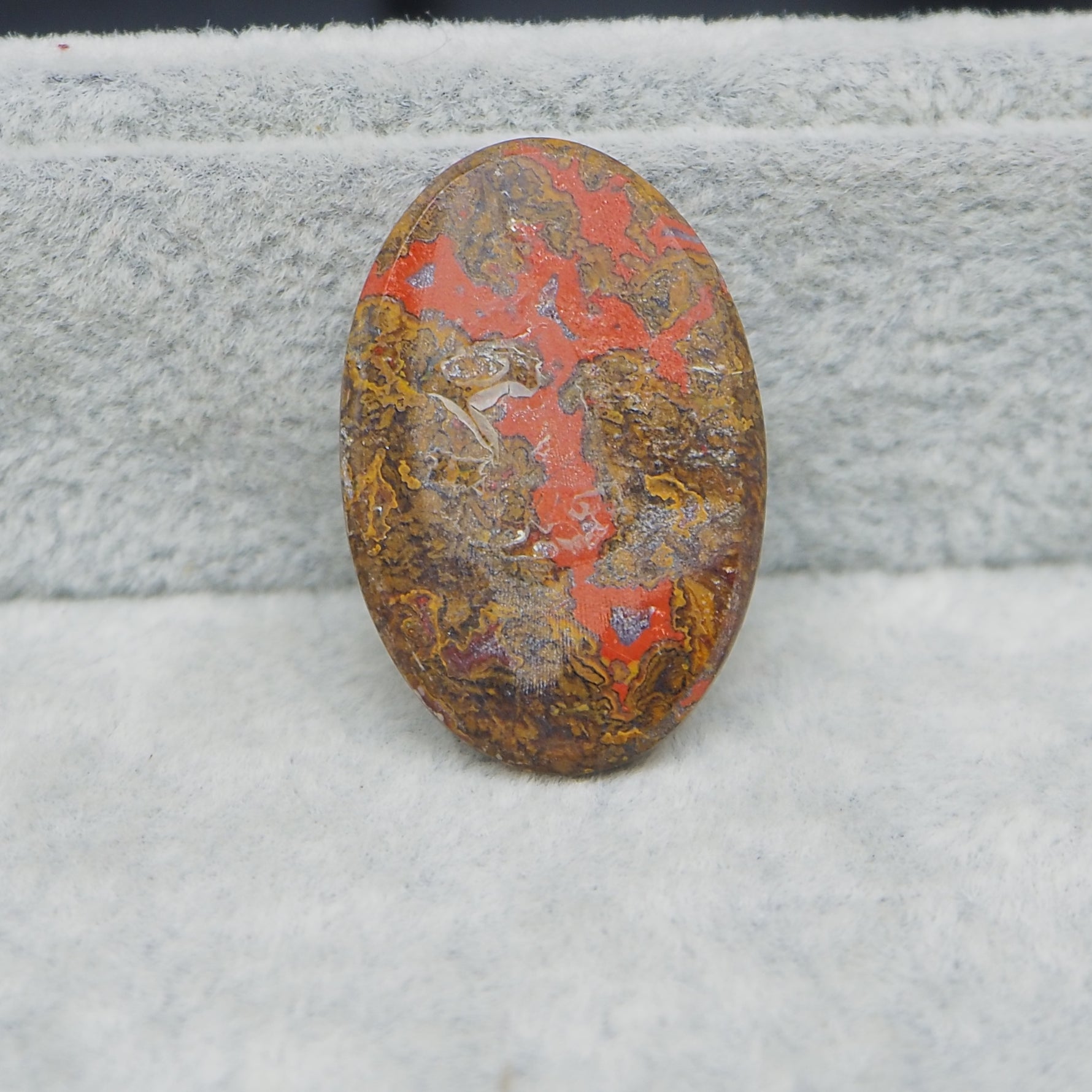 Oval-shaped stone with red and brown patterns on a textured gray background