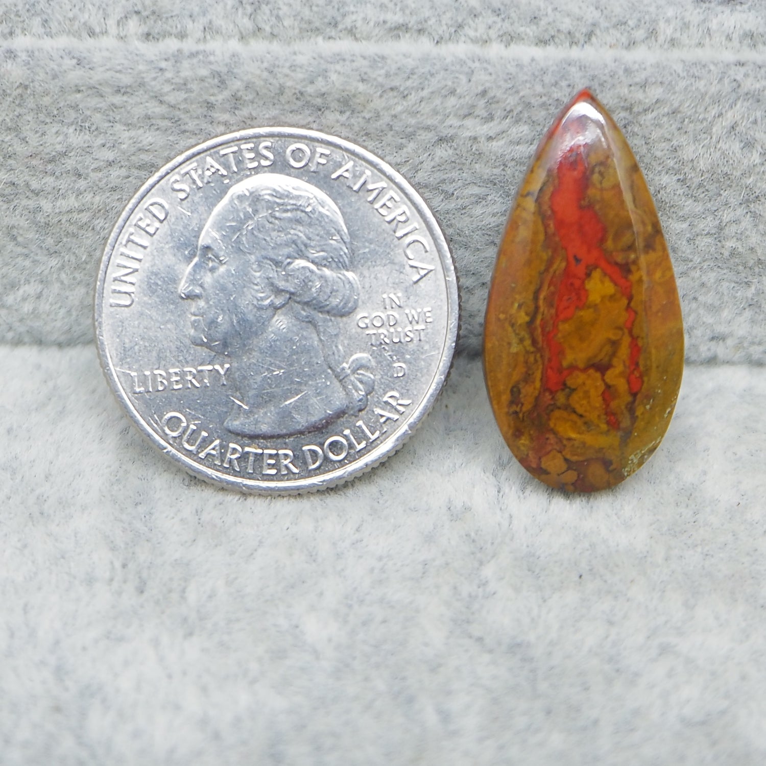 Teardrop-shaped amber stone next to a U.S. quarter dollar on a gray surface