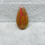 Teardrop-shaped stone with red and brown patterns on a textured gray background