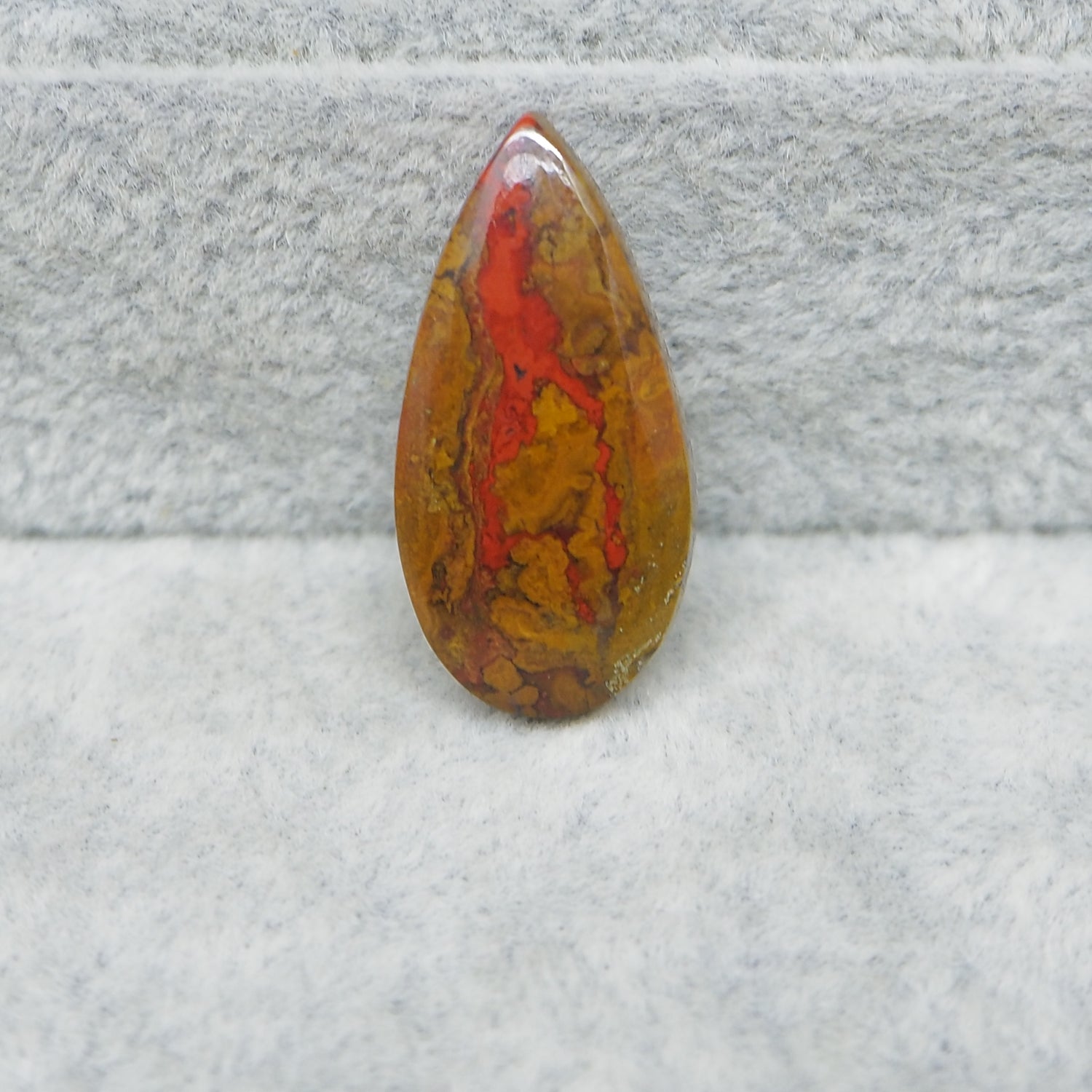 Teardrop-shaped stone with red and brown patterns on a textured gray background
