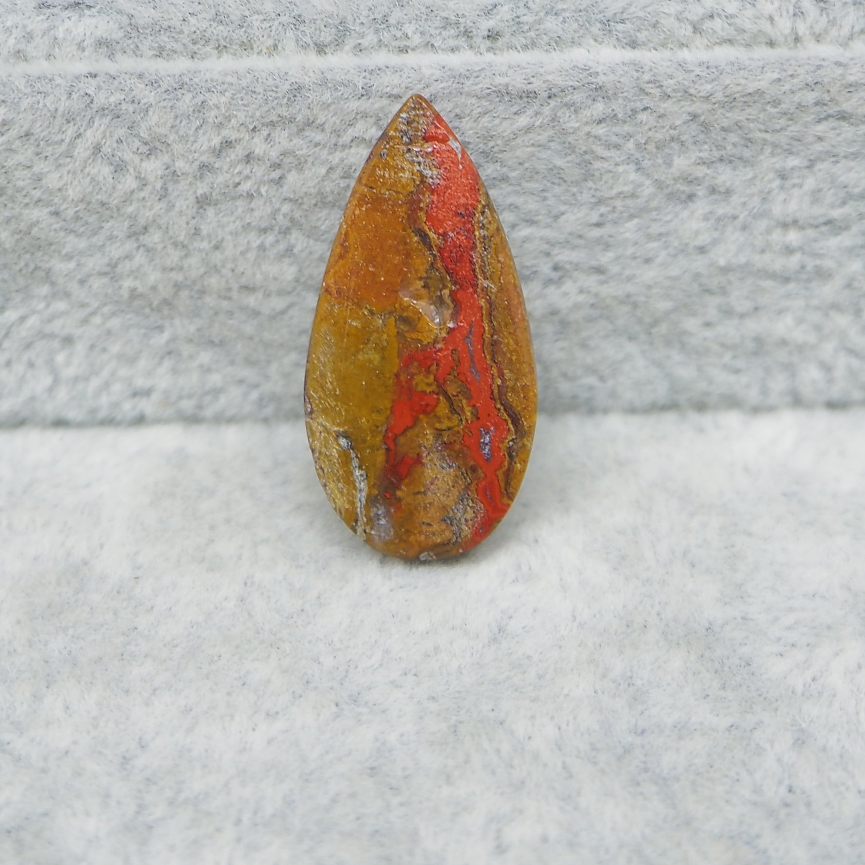 Polished stone with red and brown patterns on a textured gray surface
