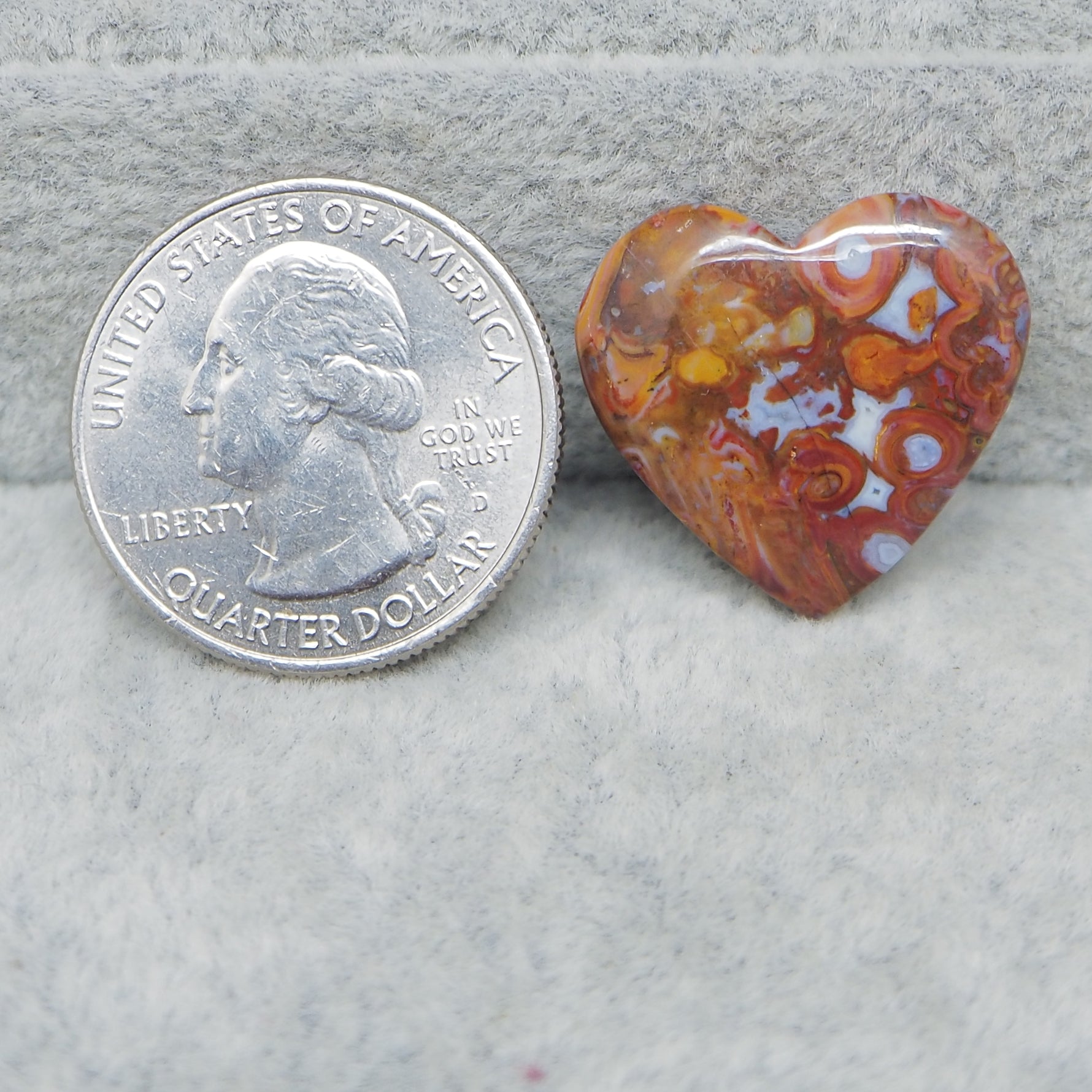 Heart-shaped agate stone next to a U.S. quarter dollar coin on a gray surface