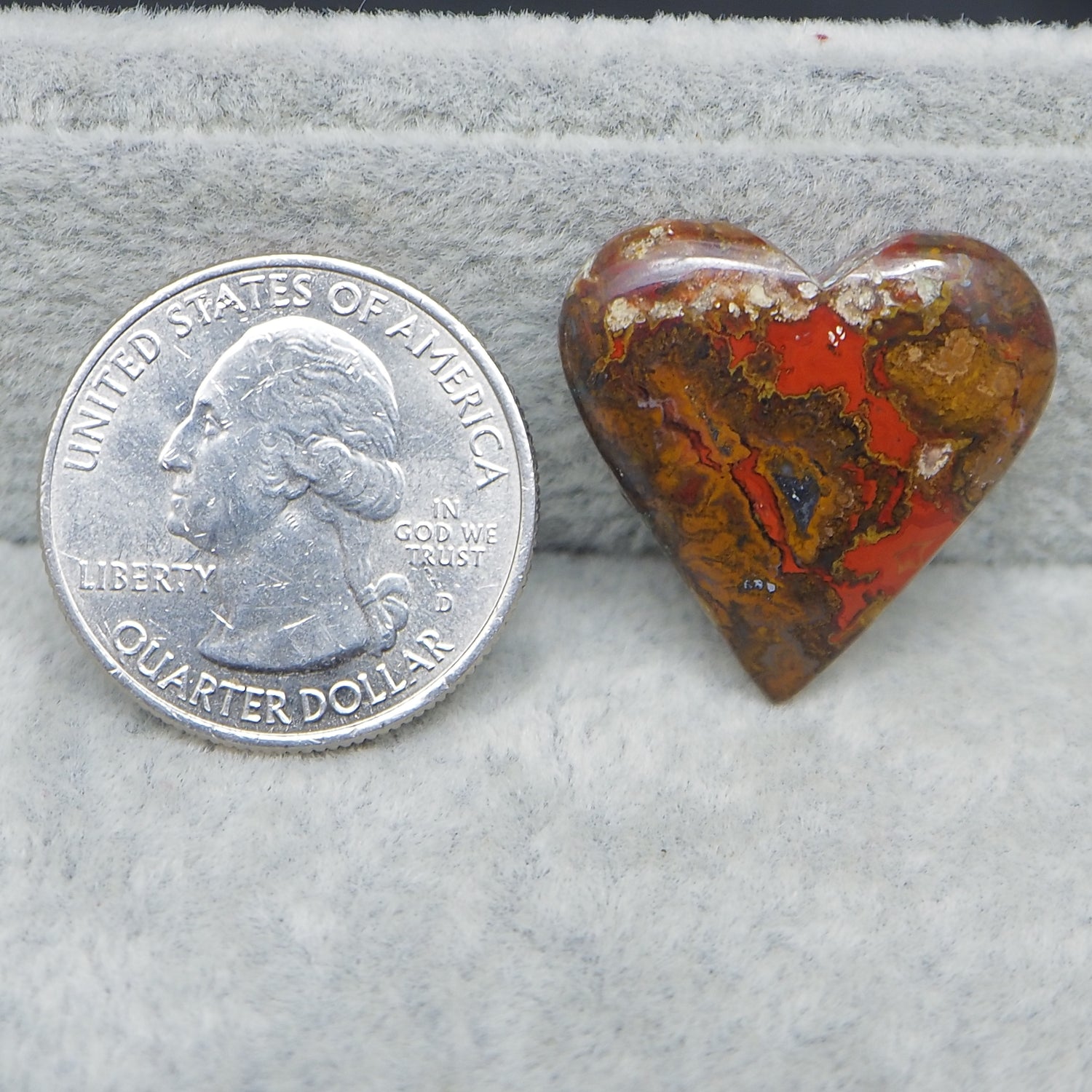 Heart-shaped stone next to a U.S. quarter dollar on a gray background