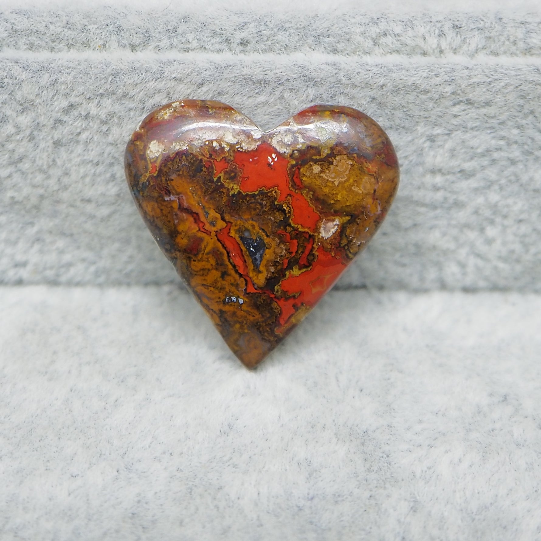 Heart-shaped stone with red and brown patterns on a gray surface