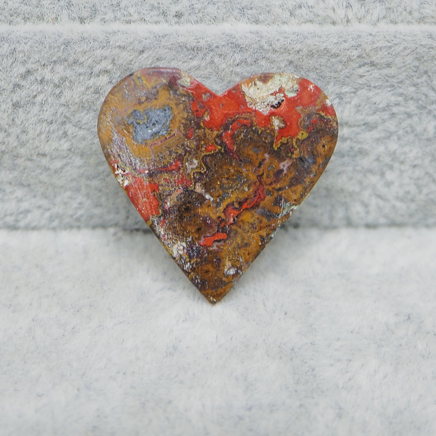 Heart-shaped stone with red and brown colors on a gray surface