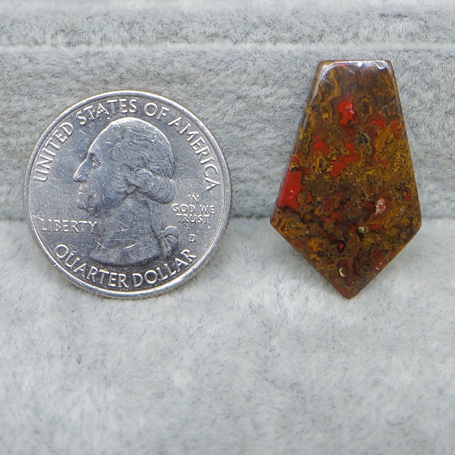Quarter dollar coin next to a red and brown stone on a gray surface
