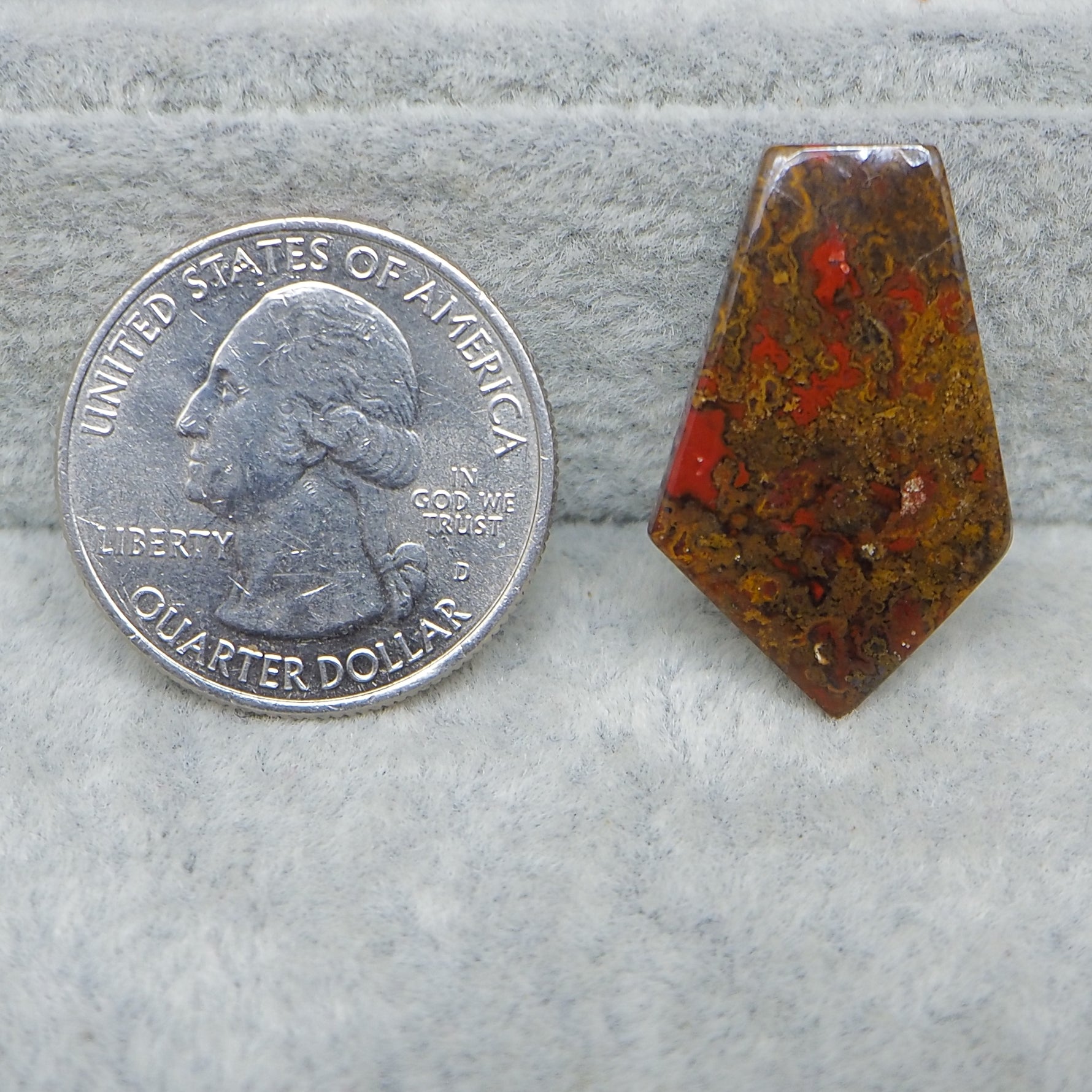 Quarter dollar coin next to a red and brown stone on a gray surface