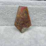 Polished stone with red and brown patterns on a textured gray surface