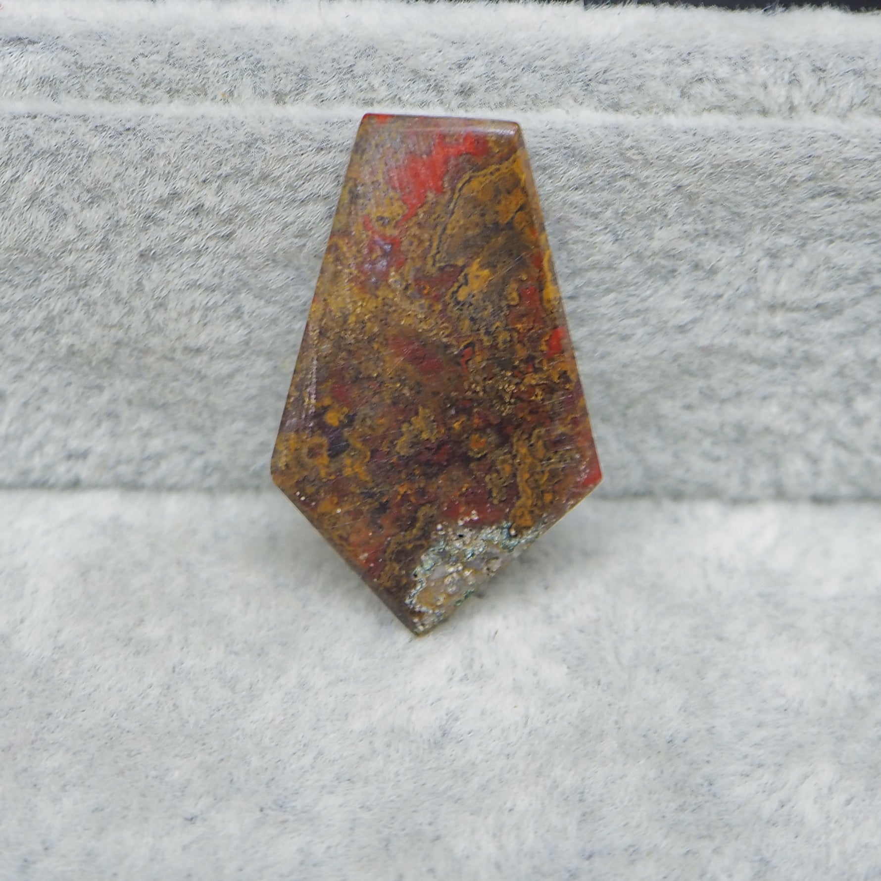 Polished stone with red and brown patterns on a textured gray surface