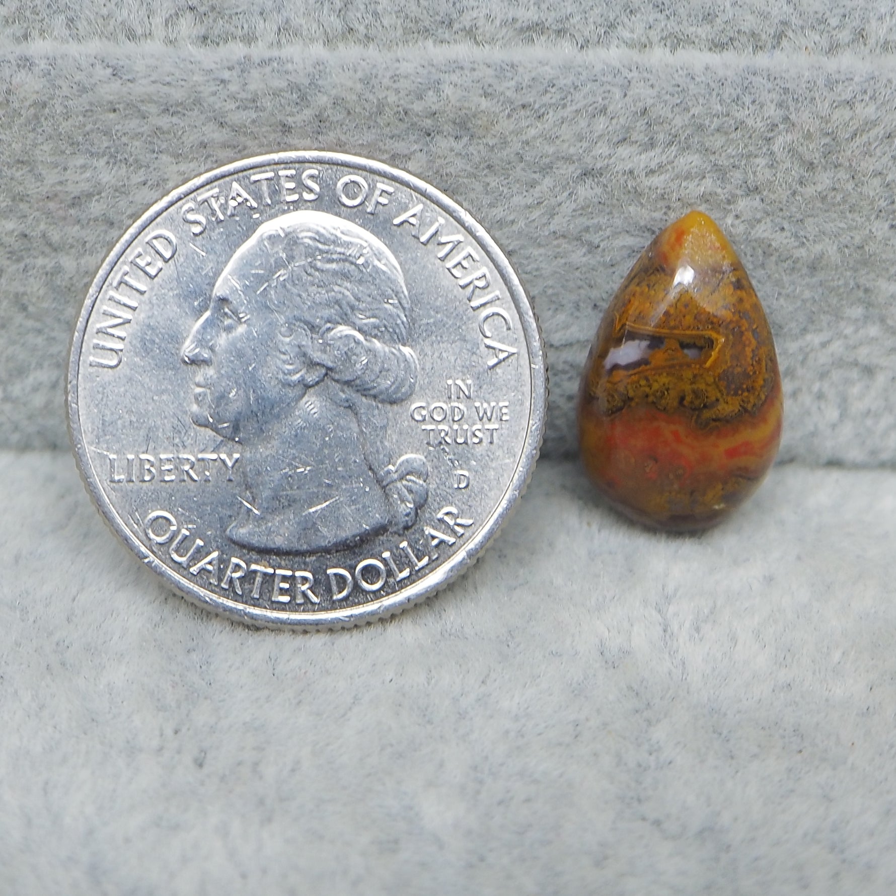 Quarter dollar coin next to a teardrop-shaped amber stone on a gray surface