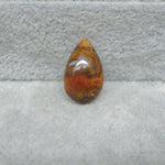Teardrop-shaped amber stone on a gray surface