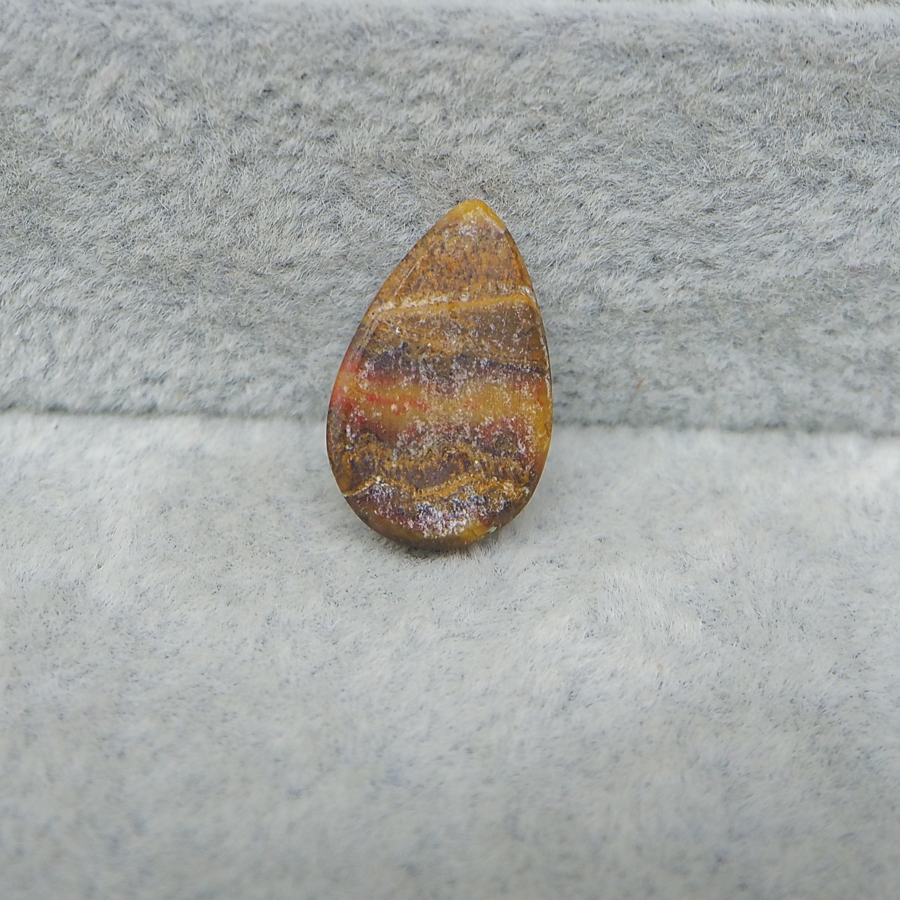 Teardrop-shaped amber stone on a gray fabric background