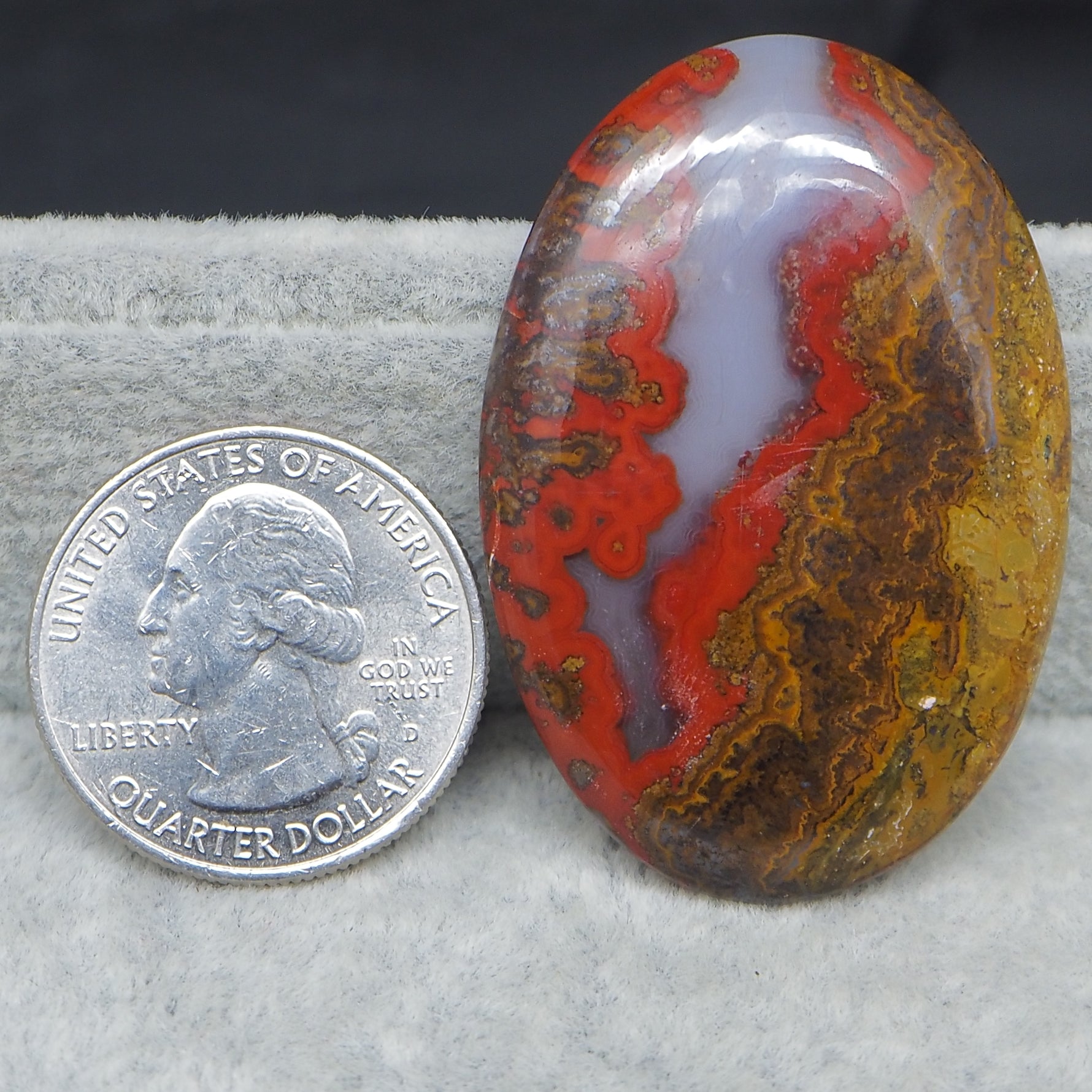 Colorful patterned stone next to a U.S. quarter dollar coin on a gray surface.