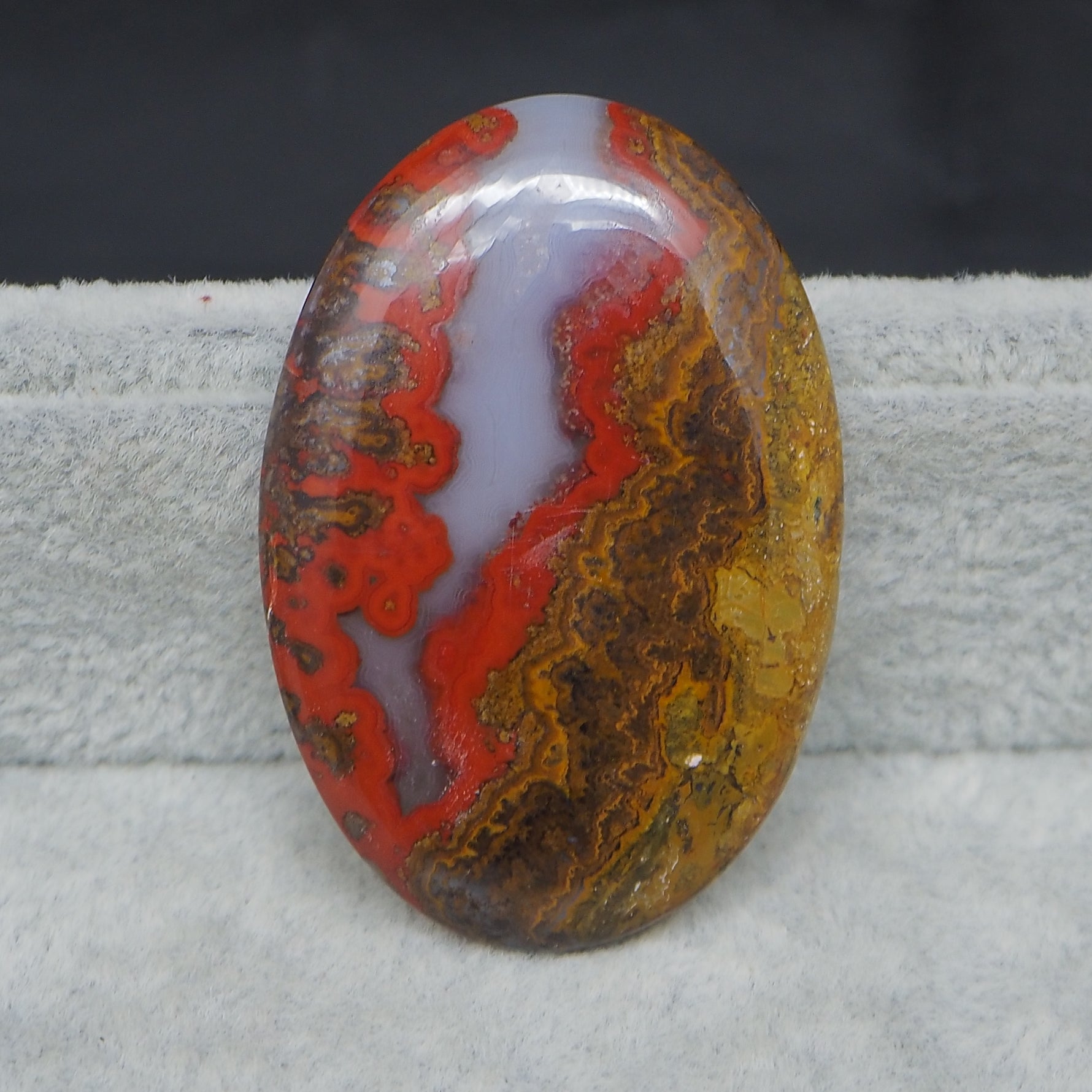 Oval-shaped agate stone with red and brown patterns on a gray surface