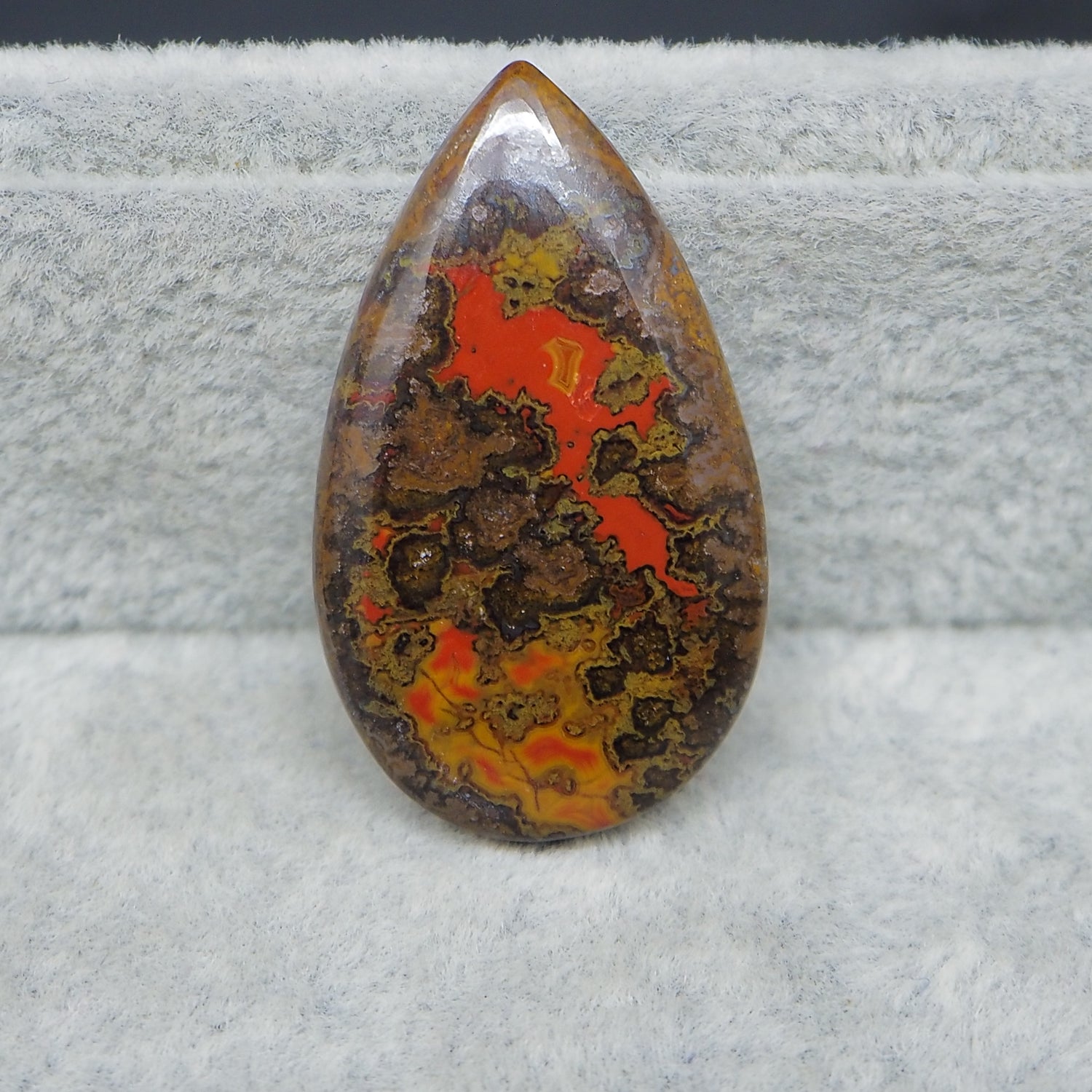 Teardrop-shaped stone with red and brown patterns on a gray surface
