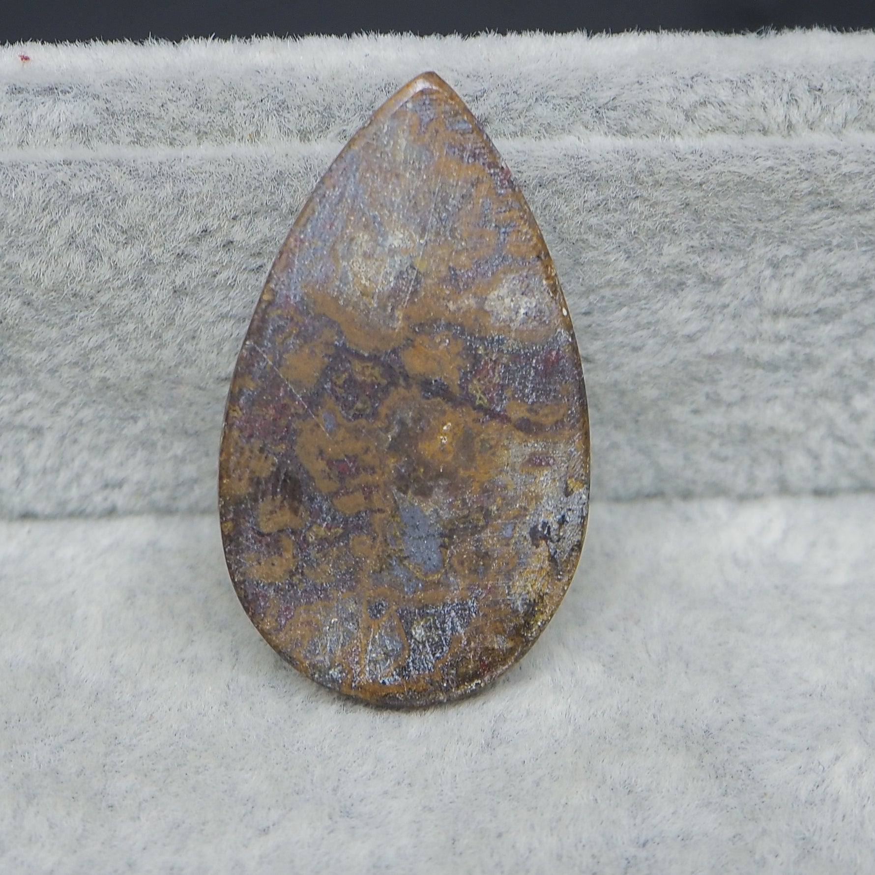 Teardrop-shaped stone with marbled pattern on a textured surface